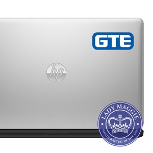 May include: A silver laptop computer with a blue sticker that says "GTE" on the top right corner. The laptop has a silver HP logo on the lid and a black bottom with the text "HEWLETT-PACKARD". A blue and white sticker with the text "LADY MAGGIE HANDCRAFTED IN THE USA" and a crown design is on the bottom right corner.