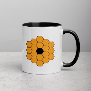 May include: White ceramic mug with a black rim and handle. The mug features a graphic of a honeycomb pattern in orange with a black center.