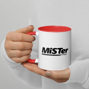 May include: White ceramic mug with a red rim and handle. The mug features a black logo that says "MiSTer FPGA".