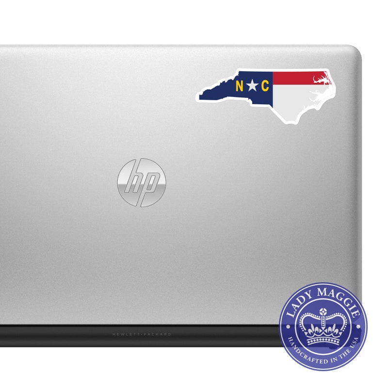 May include: A silver laptop with the HP logo on the lid. A sticker of the North Carolina state flag is on the top left corner of the lid. A blue and white sticker with the text "Lady Maggie Handcrafted in the USA" is on the bottom right corner of the laptop.