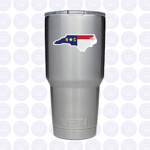 May include: A stainless steel Yeti tumbler with a North Carolina state outline sticker featuring the state flag colors and the letters "N*C".