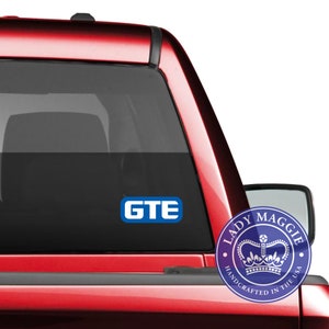 May include: A red pickup truck with a blue and white "GTE" sticker on the back window. A blue and white sticker with a crown and the text "Lady Maggie Handcrafted in the USA" is also on the window.
