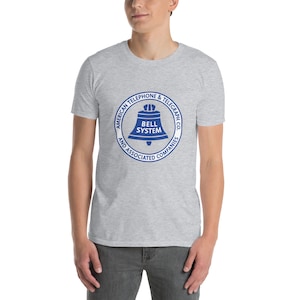 May include: A light gray t-shirt featuring a blue circular graphic with the text "AMERICAN TELEPHONE & TELEGRAPH CO. AND ASSOCIATED COMPANIES" surrounding a bell design with the words "BELL SYSTEM".