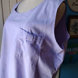 May include: A sleeveless lavender top with a small pocket on the left side. The pocket has a bow detail.