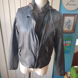 May include: A dark grey leather jacket with a zip closure and a hood. The jacket has a zipped pocket on the left side and two zipped pockets on the right side.