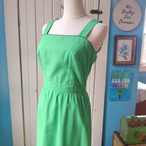 May include: A bright green sleeveless dress with a square neckline and thin black trim around the neckline and straps. The dress has a fitted bodice and a full skirt.