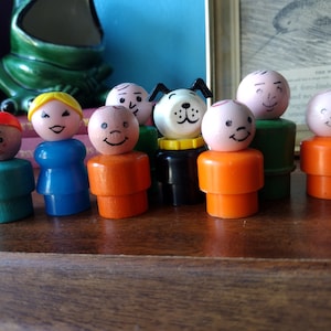 May include: A group of seven vintage plastic figurines, including a dog, standing on a wooden surface. The figurines are in various colors, including green, blue, orange, and white. The dog figurine is black with a white face and a yellow collar.