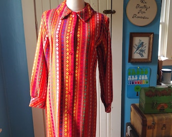May include: A long-sleeved, red dress with a colorful geometric pattern. The dress has a button-up front and a collared neckline.