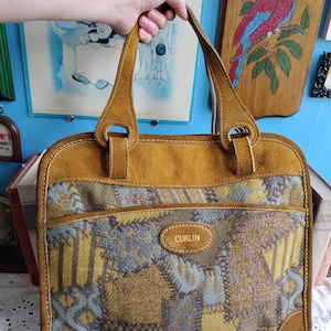 May include: A brown leather tote bag with a patchwork design in shades of blue, yellow, and brown. The bag has a suede top flap and a leather tag that reads "CURLIN".