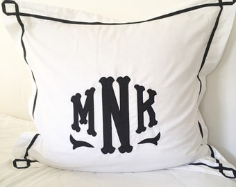 May include: White pillow with a black border and a black embroidered monogram "MNK" in the center.