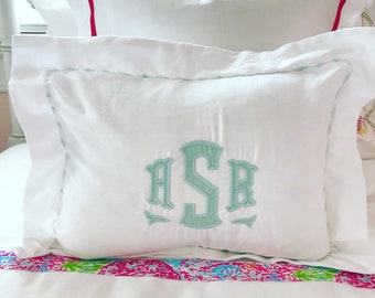 May include: White pillow with a light blue embroidered monogram "ASR" on a white bed with a pink and blue patterned bedspread.