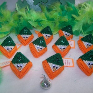 May include: A collection of 10 handmade felt ornaments shaped like leprechauns wearing green hats. The ornaments are green, orange, and white and have googly eyes. The ornaments are surrounded by green and white feathers.