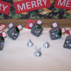 May include: Five gray felt mouse ornaments with pink ears, red berries, and green holly leaves. The ornaments are arranged in a circle around three silver foil-wrapped chocolate kisses.