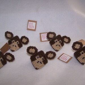 May include: Six brown and tan crocheted monkey ornaments with brown yarn ears and faces. Each ornament has a small tag attached with text that reads "squeeze my cheeks and I'll give you a kiss!"