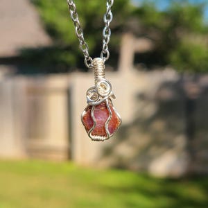 May include: A silver chain necklace with a red gemstone pendant wrapped in silver wire.