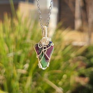 May include: A silver chain necklace with a green, pink, and red gemstone pendant wrapped in gold wire.