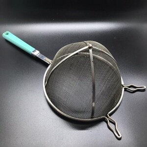 Op de afbeelding: Een zilveren zeef met een turquoise handvat. De zeef heeft een koepelvorm en een draadframe.