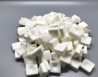 May include: A pile of white, square-shaped bath bombs. The bath bombs are arranged in a random pattern and are all the same size.