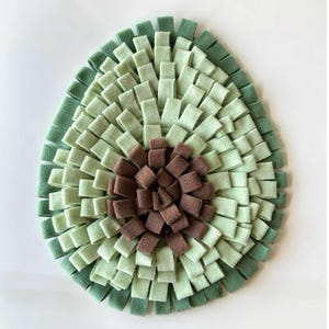 May include: A green and brown felt dog toy shaped like an avocado. The toy has a brown felt centre with green felt strips around it.