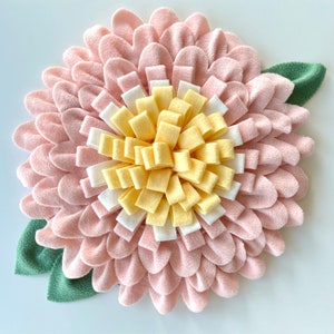 May include: A pink felt flower with a yellow and white felt center. The flower has a green felt leaf on each side.