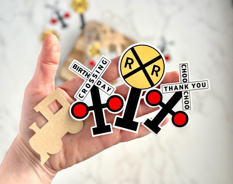 May include: A collection of train-themed stickers and cutouts. Includes a yellow and black railroad crossing sign, crossing signs with red circles, and a train-shaped cutout. Text on the stickers reads "BIRTHDAY CROSSING", "THANK YOU", and "CHOO CHOO".