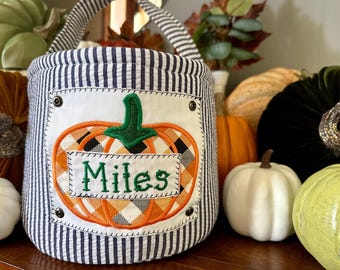 May include: A blue and white striped fabric pumpkin-shaped trick-or-treat bag with a green and orange embroidered pumpkin and the name "Miles" on it.