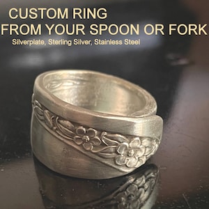 May include: A silver-toned ring crafted from a spoon or fork, featuring an embossed floral pattern along the band. The text CUSTOM RING FROM YOUR SPOON OR FORK and Silverplate, Sterling Silver, Stainless Steel is printed above the ring.