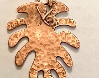 May include: A copper leaf pendant with a hammered texture. The pendant has a loop at the top for attaching a chain.