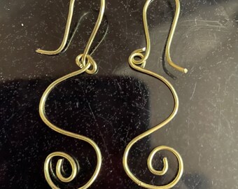 May include: A pair of gold-colored wire earrings with a unique, abstract design. The earrings are made of thin wire that is twisted and shaped into a series of loops and curves.