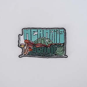 May include: An embroidered patch featuring a mermaid with long orange hair, a green tail, and a starfish in her hair. The patch displays the text "MERMAIDS SMOKE SEAWEED" in stylized lettering. The design uses shades of teal, green, orange, and black.