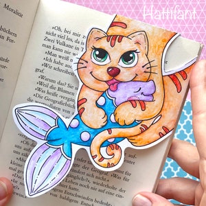 May include: A colorful bookmark featuring a cartoon cat with orange fur, green eyes, and a pink tongue. The cat is wearing a blue and white striped shirt and a purple tail. The bookmark is partially inserted into a book with German text.