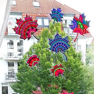 May include: Colorful patterned leaf stickers on a window with a view of a building and trees. The stickers are in shades of red, blue, green, and yellow.