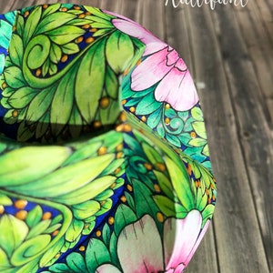 Pode incluir: Close-up de um artesanato em papel com um design floral. O artesanato apresenta folhas verdes, flores rosa e detalhes dourados sobre um fundo azul. A palavra "Hattifant" est&aacute; escrita em branco.
