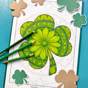 May include: A printable colouring page featuring a detailed shamrock design with green, blue and white colours. The shamrock is surrounded by a mandala pattern. The image includes the text "Hattifant Design".