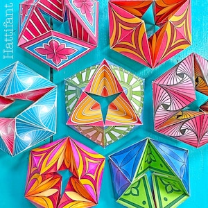May include: A collection of seven folded paper geometric sculptures featuring vibrant, multi-colored patterns including floral, radial, and striped designs. Each hexagonal structure displays intricate symmetry and the text Hattifant.