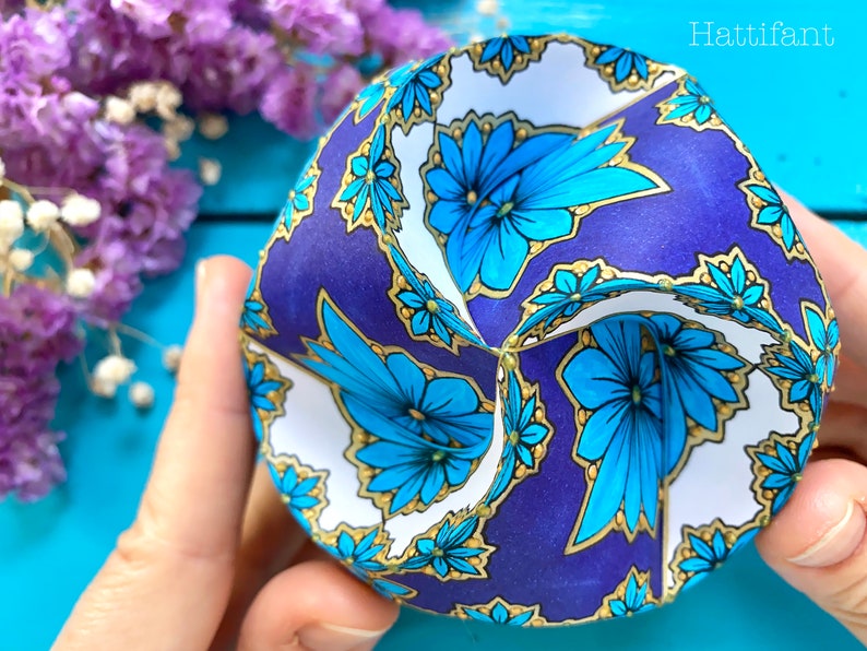 May include: A paper sphere with a blue, gold, and white floral pattern. The sphere is folded into a geometric shape.