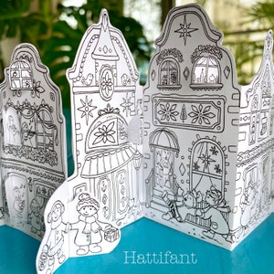 May include: A black and white printable papercraft of a Christmas village with three houses, each with a unique design. The houses have windows, doors, and decorative details. There are two people standing in front of the houses, and a cat is walking by.
