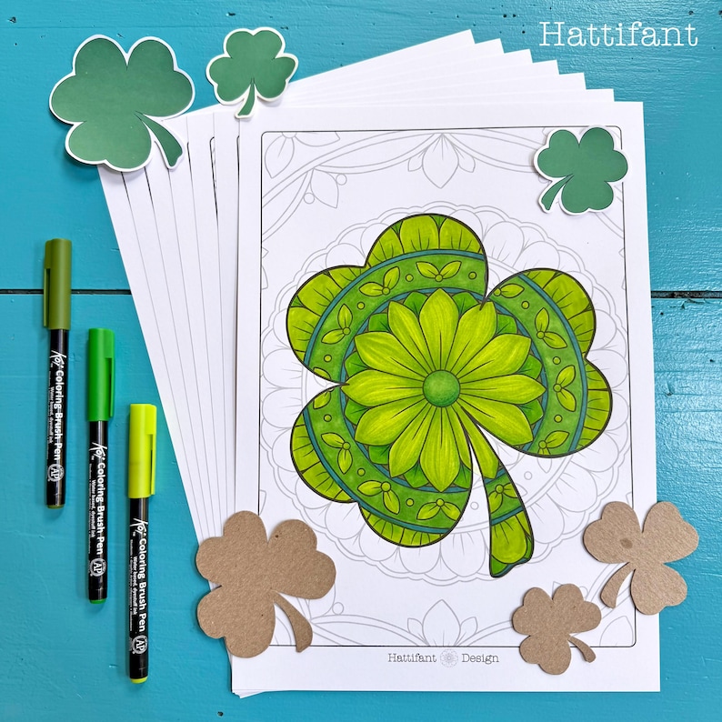 May include: A stack of printable colouring pages featuring a green shamrock with intricate mandala designs. The pages are surrounded by green shamrock cutouts and green markers.