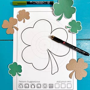 May include: A printable colouring page featuring a shamrock with a grid pattern. The page includes pattern suggestions and space to add your own designs. The text "Hattifant Design" is at the bottom of the page.