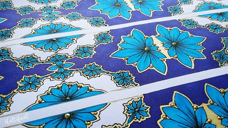 May include: Four strips of paper with a repeating pattern of blue flowers with gold accents on a purple background. The flowers have a white center and are outlined in black. The paper is decorated with gold glitter.