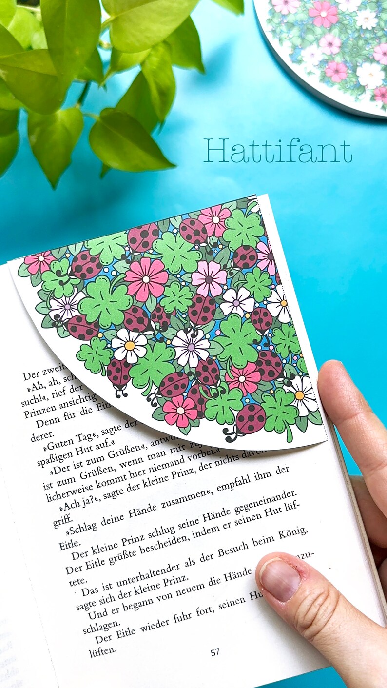 May include: A close-up of a book with a bookmark featuring a colorful floral design with ladybugs. The text on the page reads "Hattifant" and includes a German story about a prince.
