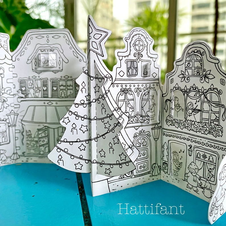 May include: A black and white printable paper craft of a Christmas village with a Christmas tree in the center. The village has four buildings with windows and doors. The buildings are decorated with Christmas lights and ornaments. The text "Hattifant" is printed at the bottom of the image.