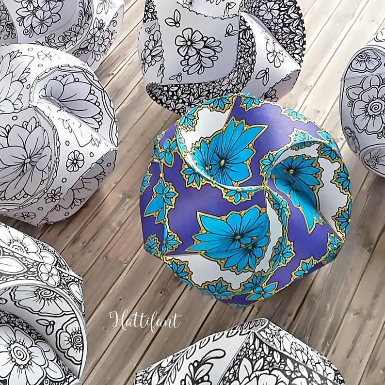 May include: Five paper mache spheres with different floral patterns. The spheres are white with black and blue floral designs. The spheres are sitting on a wooden surface. The word "Hattifant" is written on the surface.
