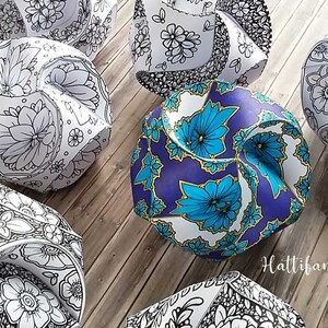 May include: A collection of eight origami paper balls with intricate floral designs. The balls are in various shades of white, black, blue, and gold. The balls are arranged on a wooden surface.