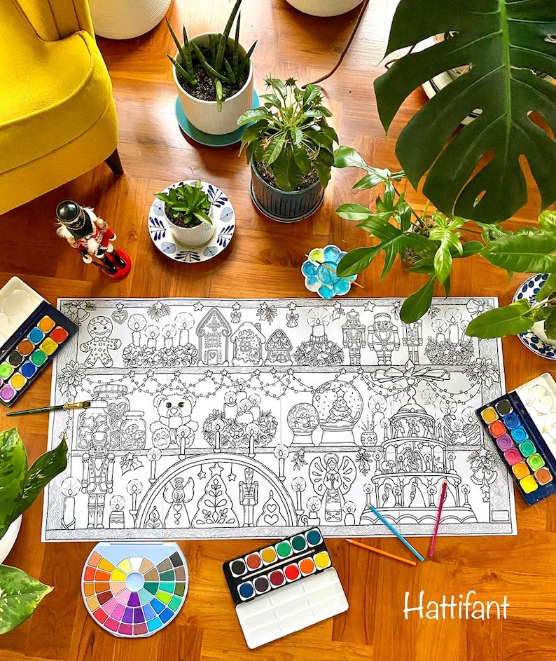 May include: A black and white coloring page featuring a Christmas scene with gingerbread houses, nutcrackers, and a carousel. The page is surrounded by paintbrushes, watercolors, and a color wheel.