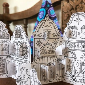May include: A black and white printable paper craft advent calendar featuring a row of houses with doors and windows. The houses are decorated with stars, snowflakes, and other festive details. The calendar is designed to be cut out and assembled.