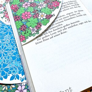 May include: A book with a floral bookmark. The bookmark is a light blue background with pink, white, and green flowers and red ladybugs. The book is titled "Hattifant".