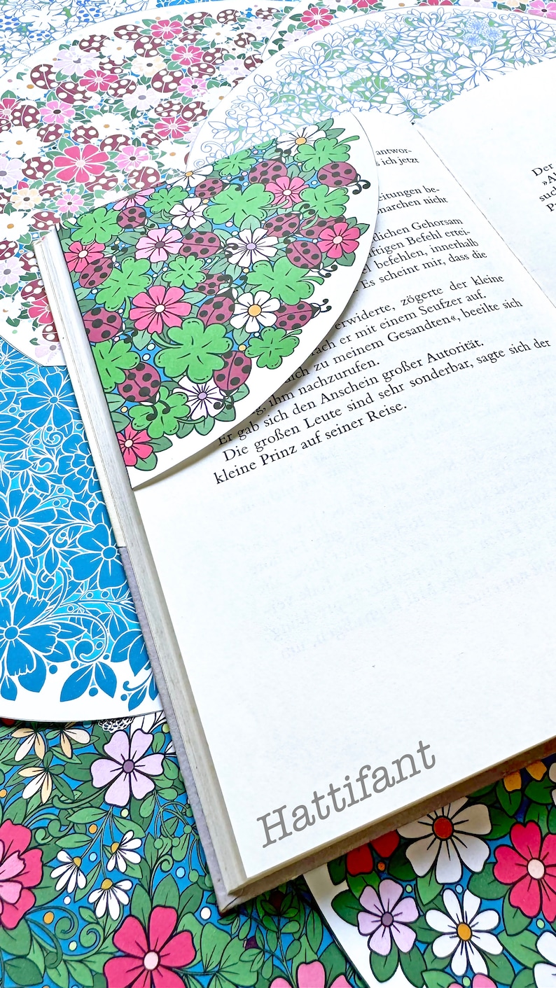 May include: A book with a floral bookmark. The bookmark is a light blue background with pink, white, and green flowers and red ladybugs. The book is titled "Hattifant".