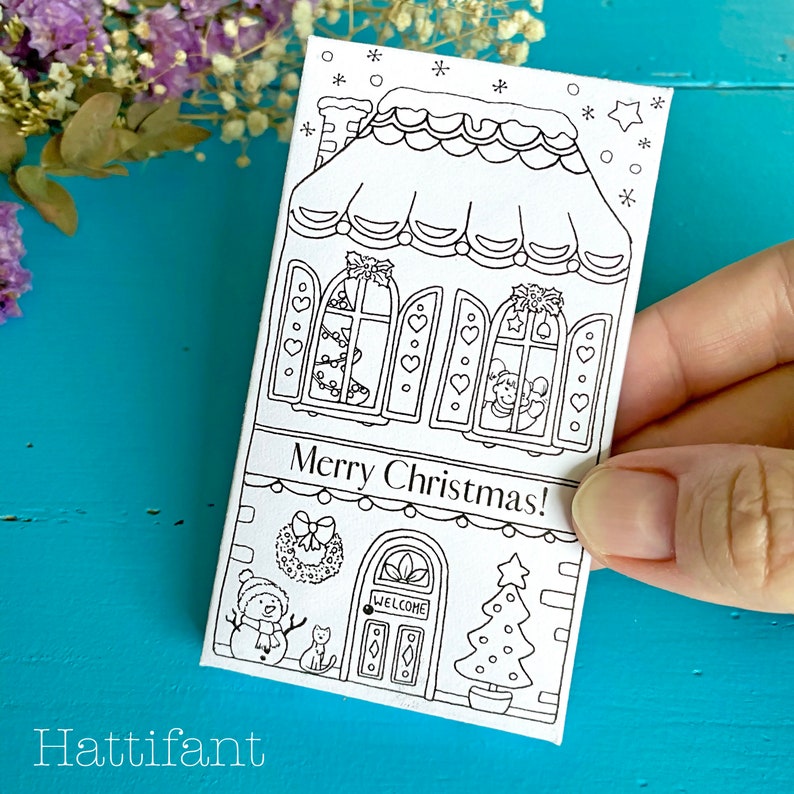May include: A black and white coloring page featuring a gingerbread house with a snowman, cat, and Christmas tree. The text "Merry Christmas!" is written on the house.