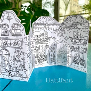 May include: A black and white printable papercraft of a gingerbread house with a star on top. The house has windows, a door, and a balcony. The text "Hattifiant" is printed below the house.